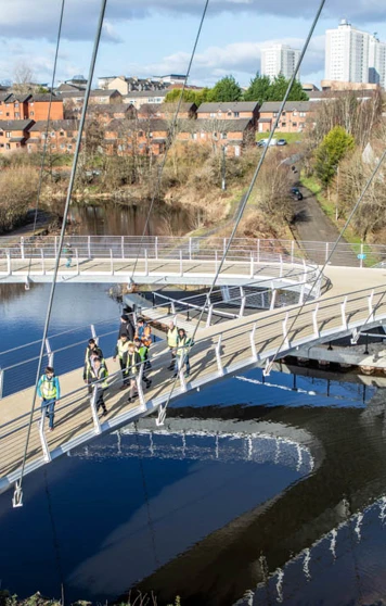 Overhead view of students and lecturers walking across the curved paths of the Stockingfield Bridge, with the canal reflecting the structure and surrounding landscape. Overhead view of students and lecturers walking across the curved paths of the Stockingfield Bridge, with the canal reflecting the structure and surrounding landscape.